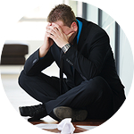 A man in a suit sits on the floor with his head in his hands.